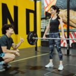 Mulher realizado exercício com barra, que exige muita postura.